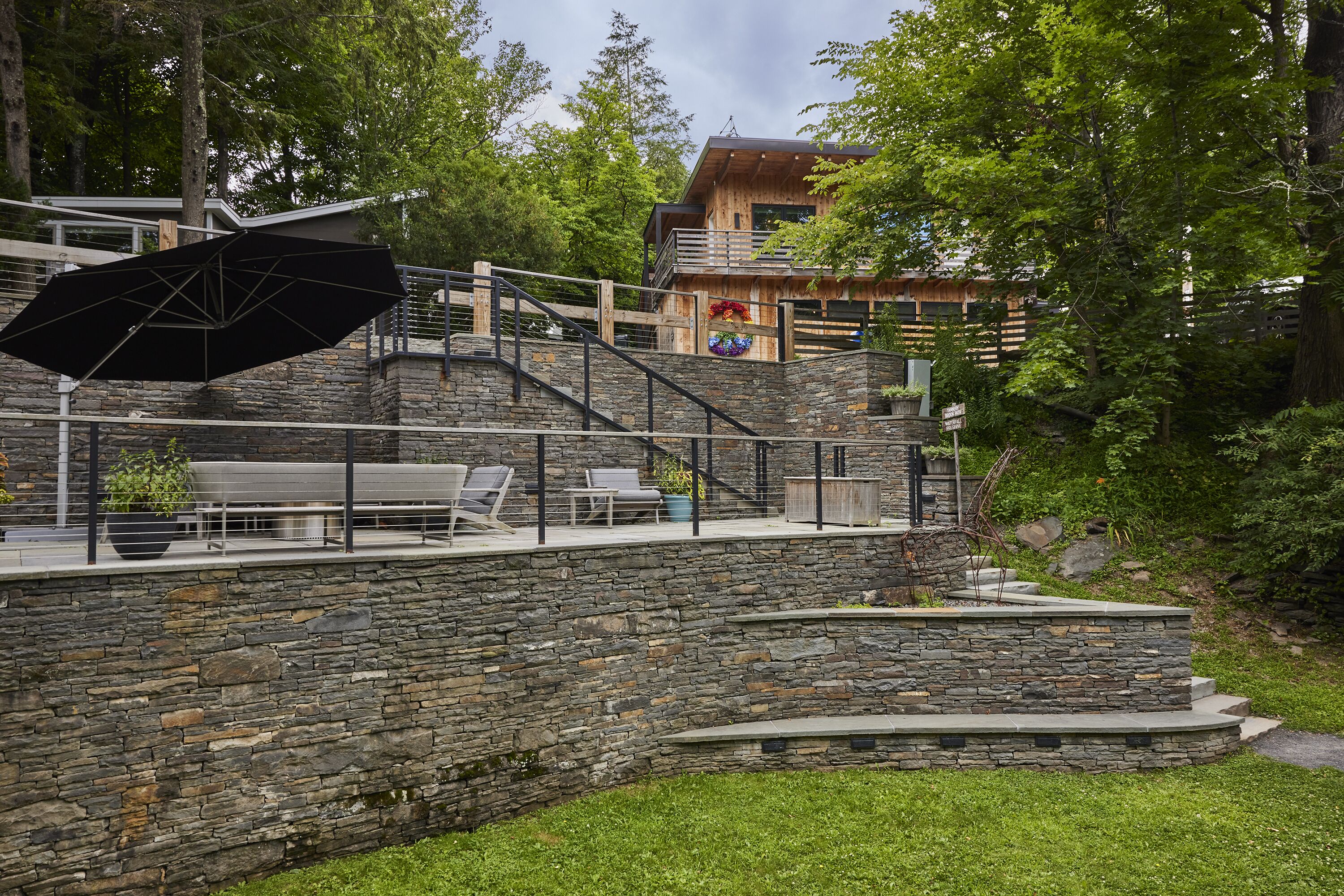 A stone staircase leading to a wooden deck with outdoor furniture and a large umbrella.
