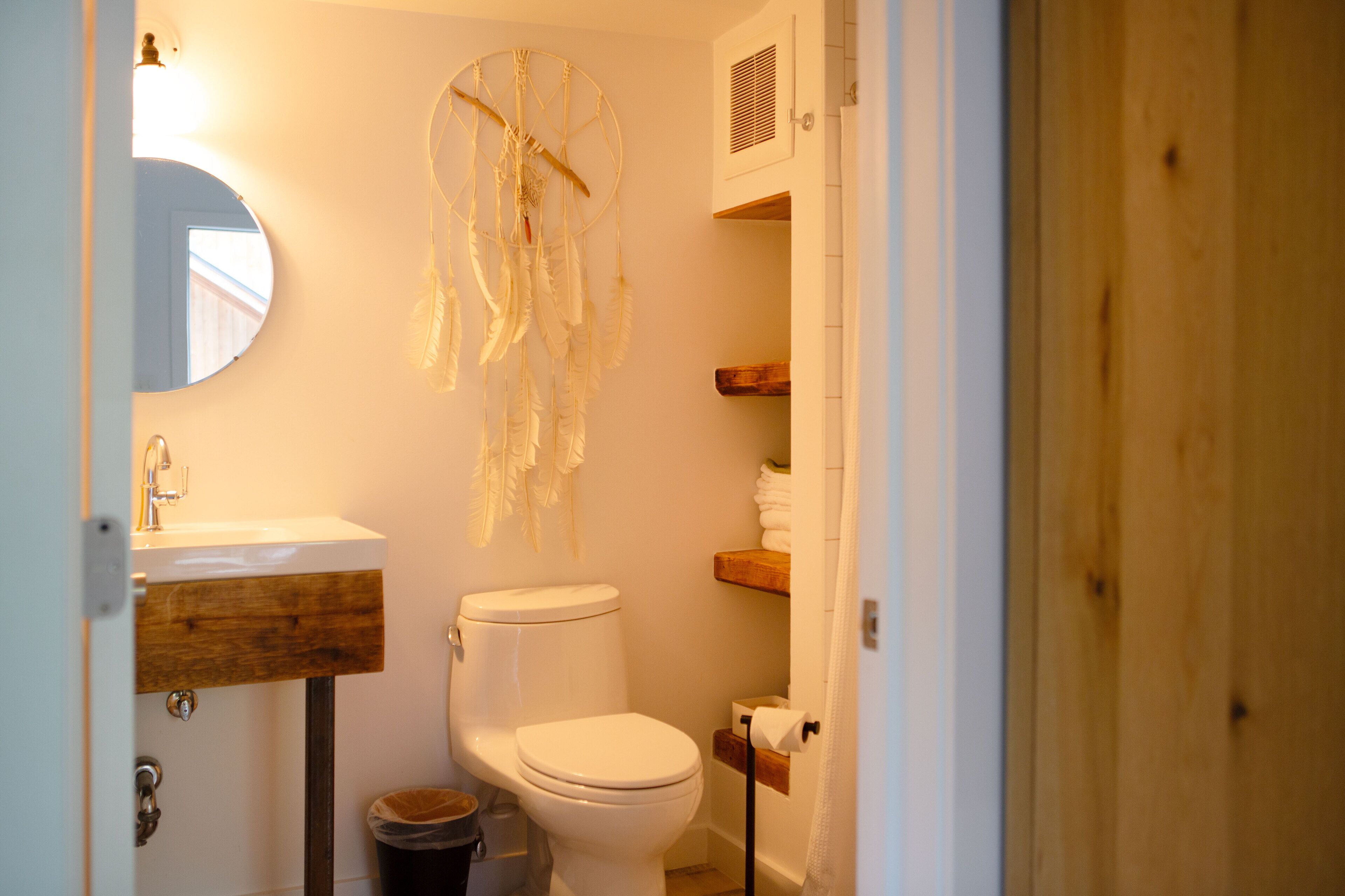 A bathroom with a white toilet, a wooden vanity, a dreamcatcher, and a mirror.
