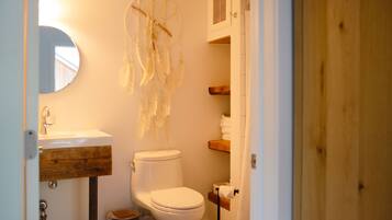 A bathroom with a white toilet, a wooden vanity, a dreamcatcher, and a mirror.