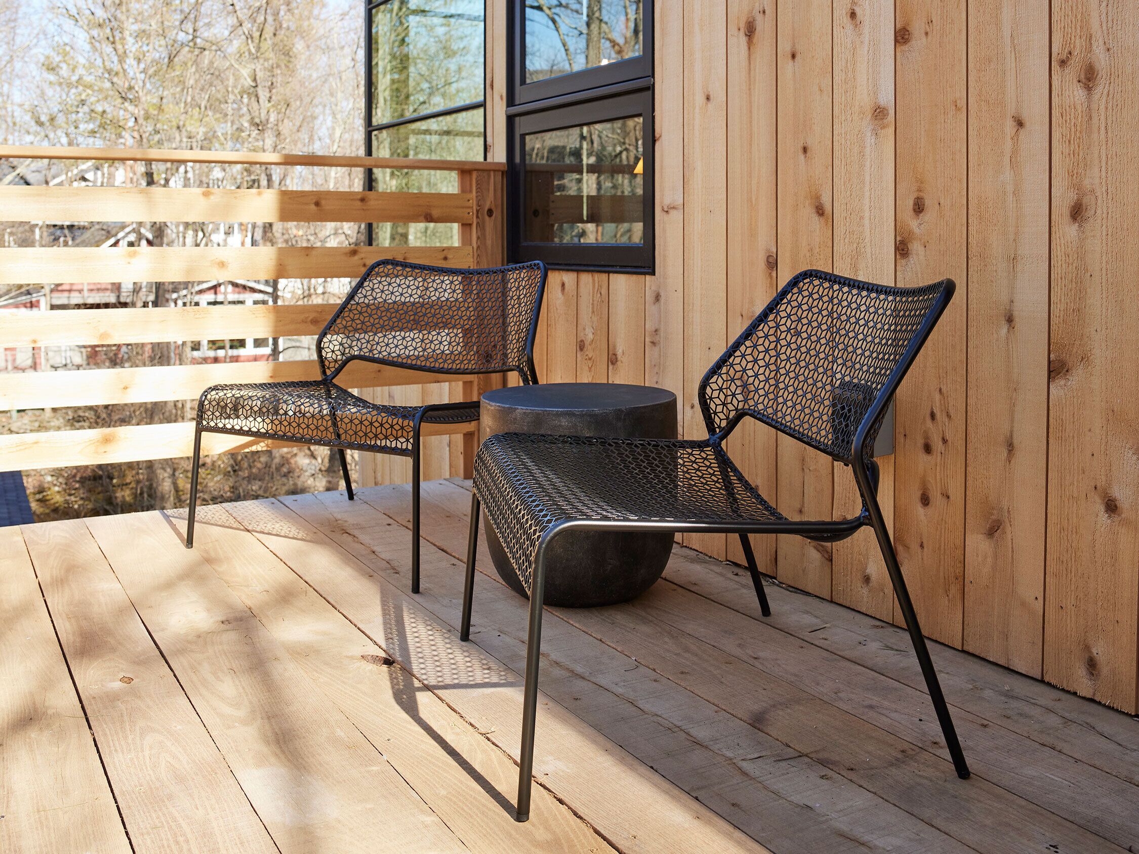 Una terraza de madera con dos sillas de metal y una mesa redonda.
