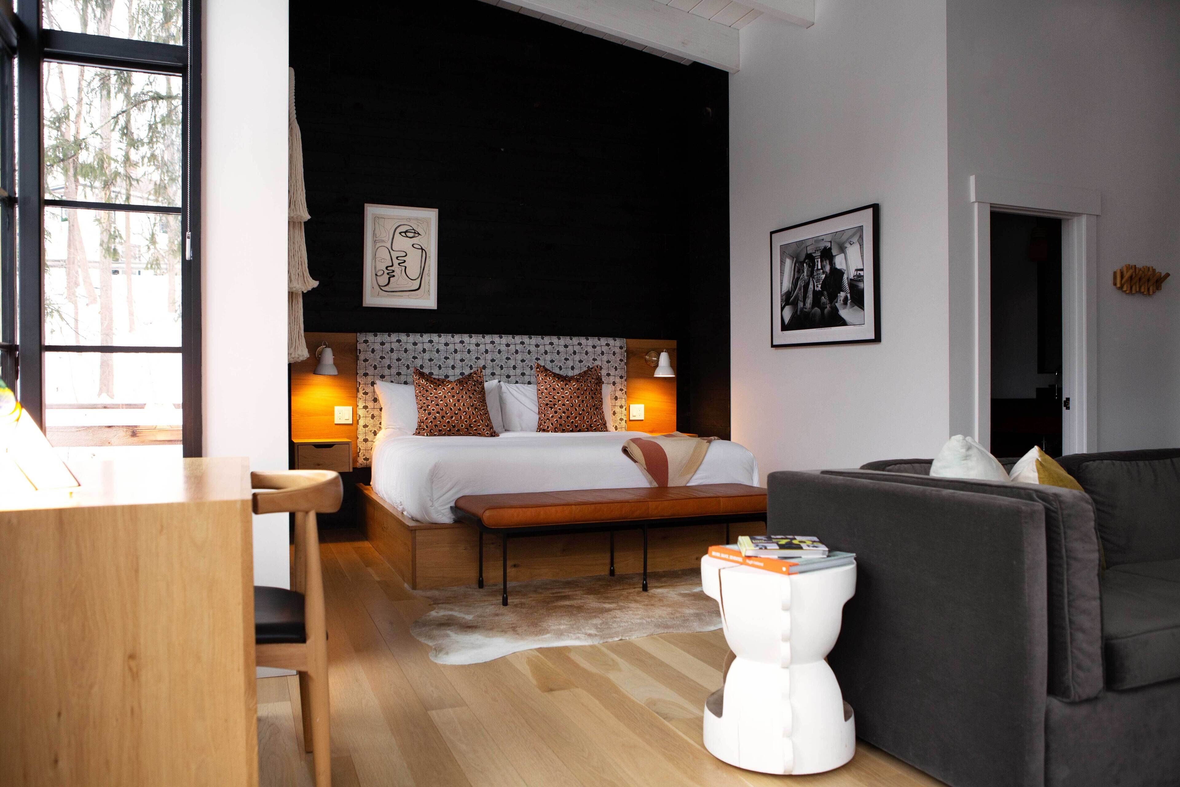 A modern bedroom with a large bed, a wooden desk, a grey sofa, and a white toilet.