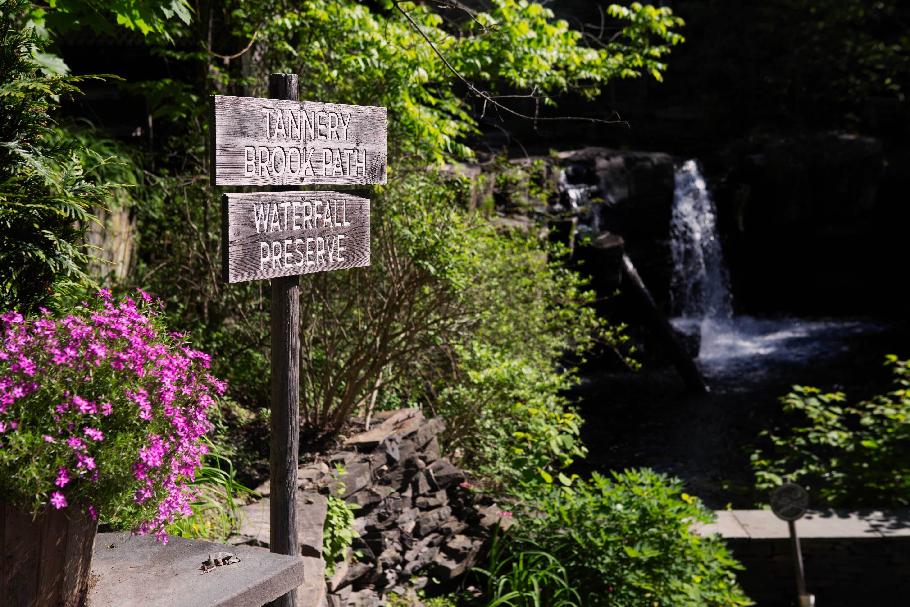 Een houten bord met aanduidingen naar 'Tanery Brook Path' en 'Waterfall Preserve'.