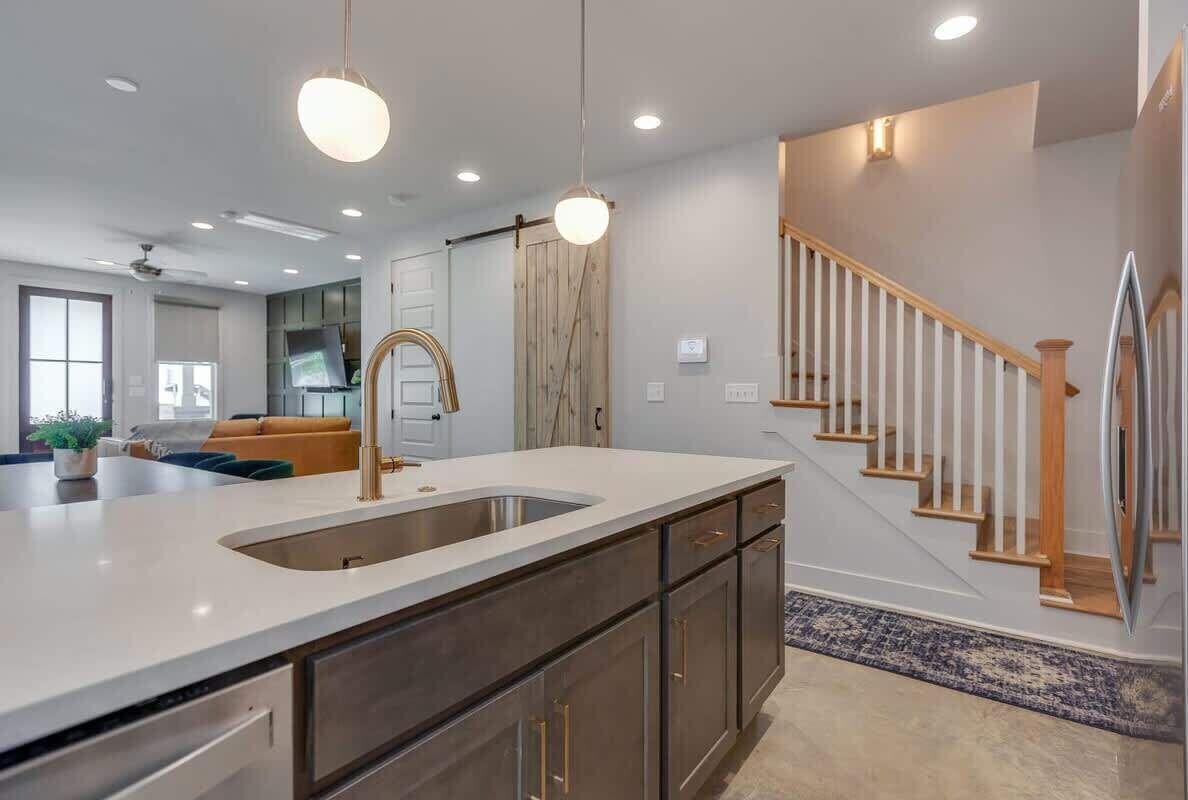 A modern kitchen with a large island, stainless steel appliances, and a wooden staircase.