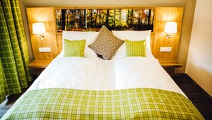 A hotel room with a large bed, two nightstands, a headboard with a forest mural, and two wall-mounted lamps. - Der Dorfwirt (Rechberg)