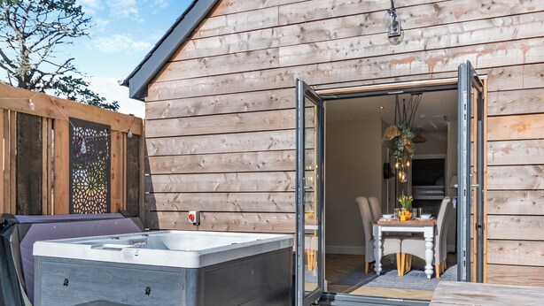 A wooden exterior with a hot tub and a table with chairs outside a building.