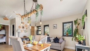 A modern living room with a wooden dining table, grey sofa, and a hanging light fixture.