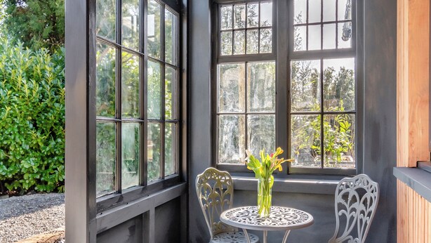 A room with two ornate metal chairs and a small round table with a vase of flowers. Large windows with multiple panes allow natural light to enter. - 2 bedroom accommodation in Goodwick, near Fishguard (Goodwick, near Fishguard)