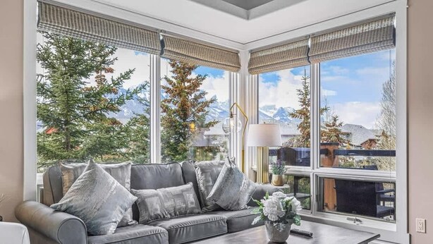 A modern living room with a grey sofa, a coffee table, and large windows offering a mountain view.