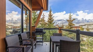 A balcony with wicker furniture, a grill, and a view of mountains.