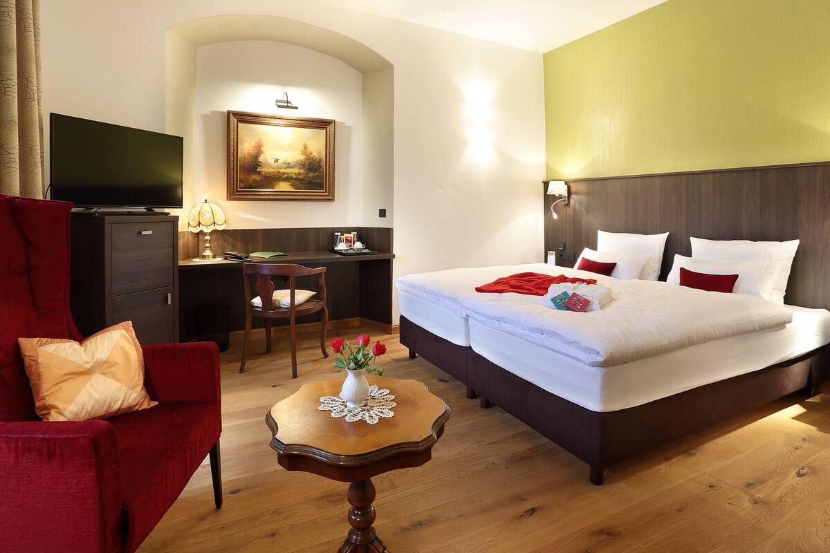 A hotel room with a bed, a desk, a TV, a chair, and a small table with a vase of flowers.