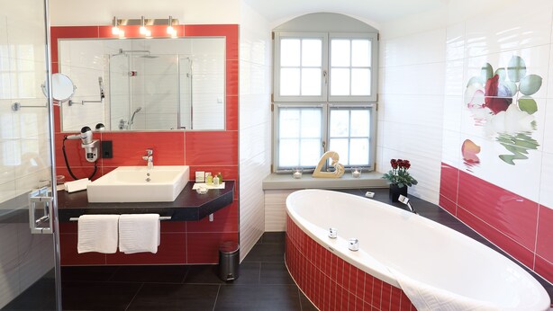 A modern bathroom with a large mirror, a sink, a bathtub, and a window with a view. - Schloß Schönberg (Bad Brambach)