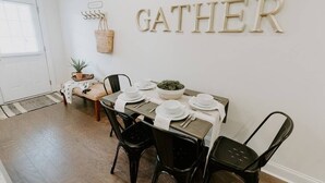 Un coin repas avec une table dressée pour quatre personnes, un panneau «RASSEMBLEMENT» accroché au mur et un panier posé sur le sol.