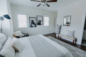 Ein Schlafzimmer mit Bett, einer Bank, einem Schreibtisch, einem Stuhl, einem Deckenventilator und gerahmten Bildern an der Wand.