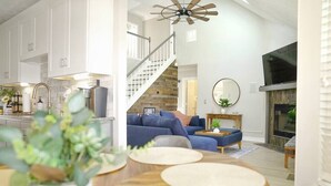 A spacious living area with a staircase leading to an upper level, a fireplace, and a large TV.