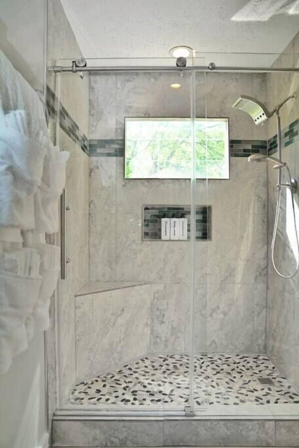 A modern shower area with a glass door, a mounted TV, and a showerhead.