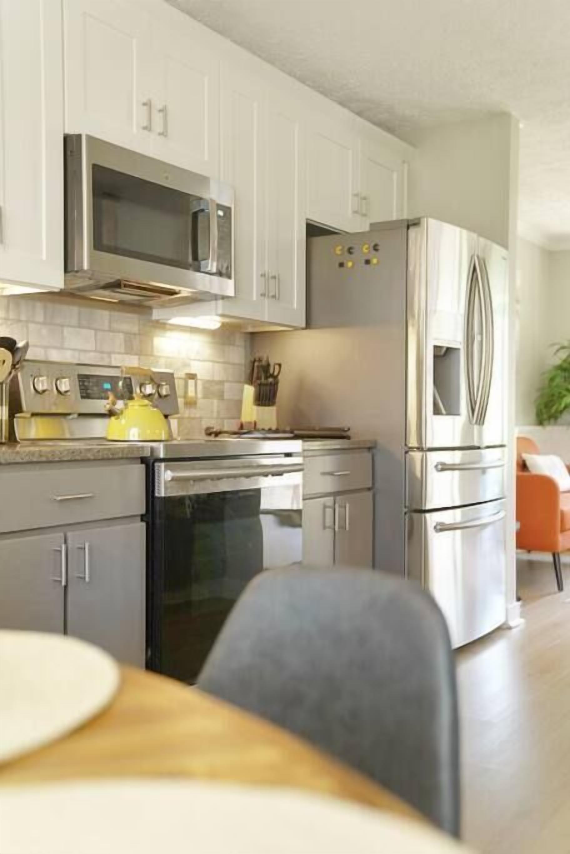 A modern kitchen with stainless steel appliances, white cabinetry, and a dining area with a table and chairs.