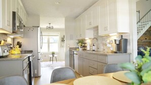 A modern kitchen with white cabinets, a dining area with a round table, and a staircase leading to an upper level.