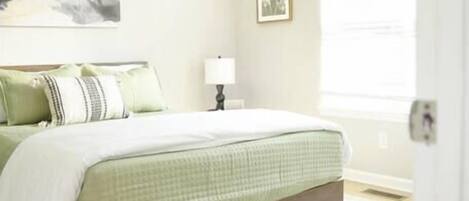 A bedroom with a bed, a ceiling fan, a nightstand, a lamp, a framed picture on the wall, and a window with blinds.