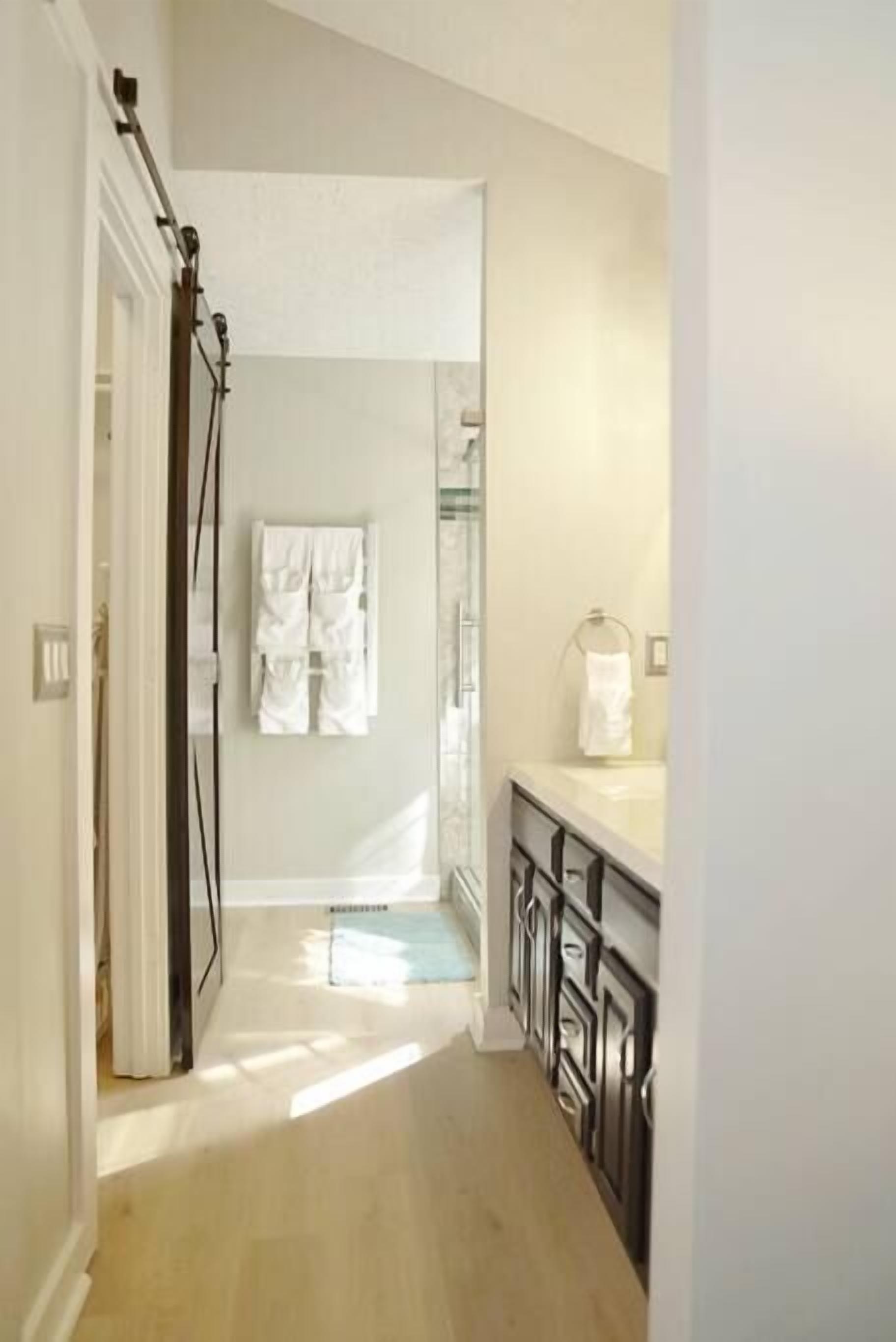 A hallway leading to a bathroom with a shower, a toilet, and a sink. There are towels hanging on the wall.