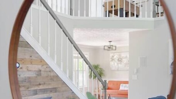A round mirror reflecting a living room with a staircase, a sofa, and a plant.