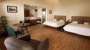 A hotel room with two beds, a sitting area with a chair and table, a bathroom with a mirror, and a potted plant. - Sublime Valley Resort (Villa de Allende)