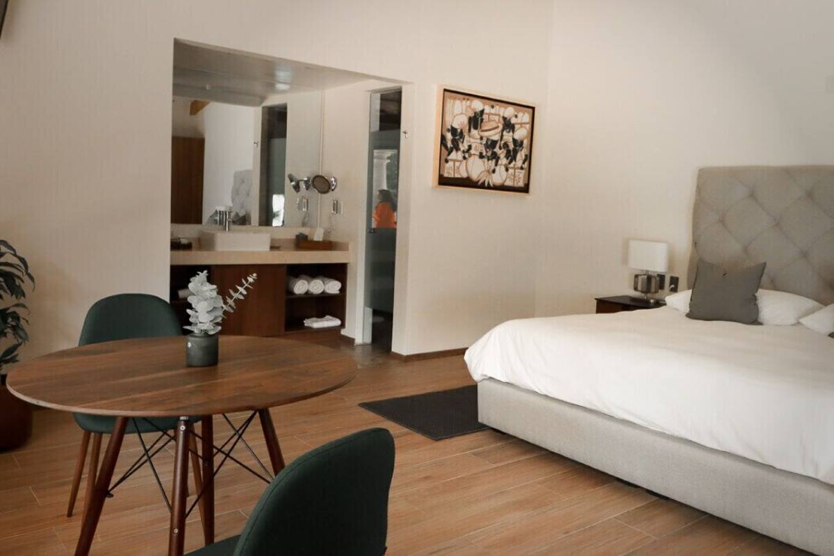 A hotel room with a large bed, a round dining table, and a potted plant.