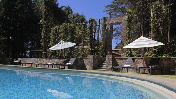 A swimming pool with lounge chairs and umbrellas, surrounded by stone structures and trees. - Sublime Valley Resort (Villa de Allende)
