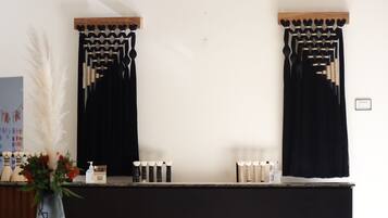 Un baño con cortinas negras, un estante de madera con artículos de aseo y un florero con flores.