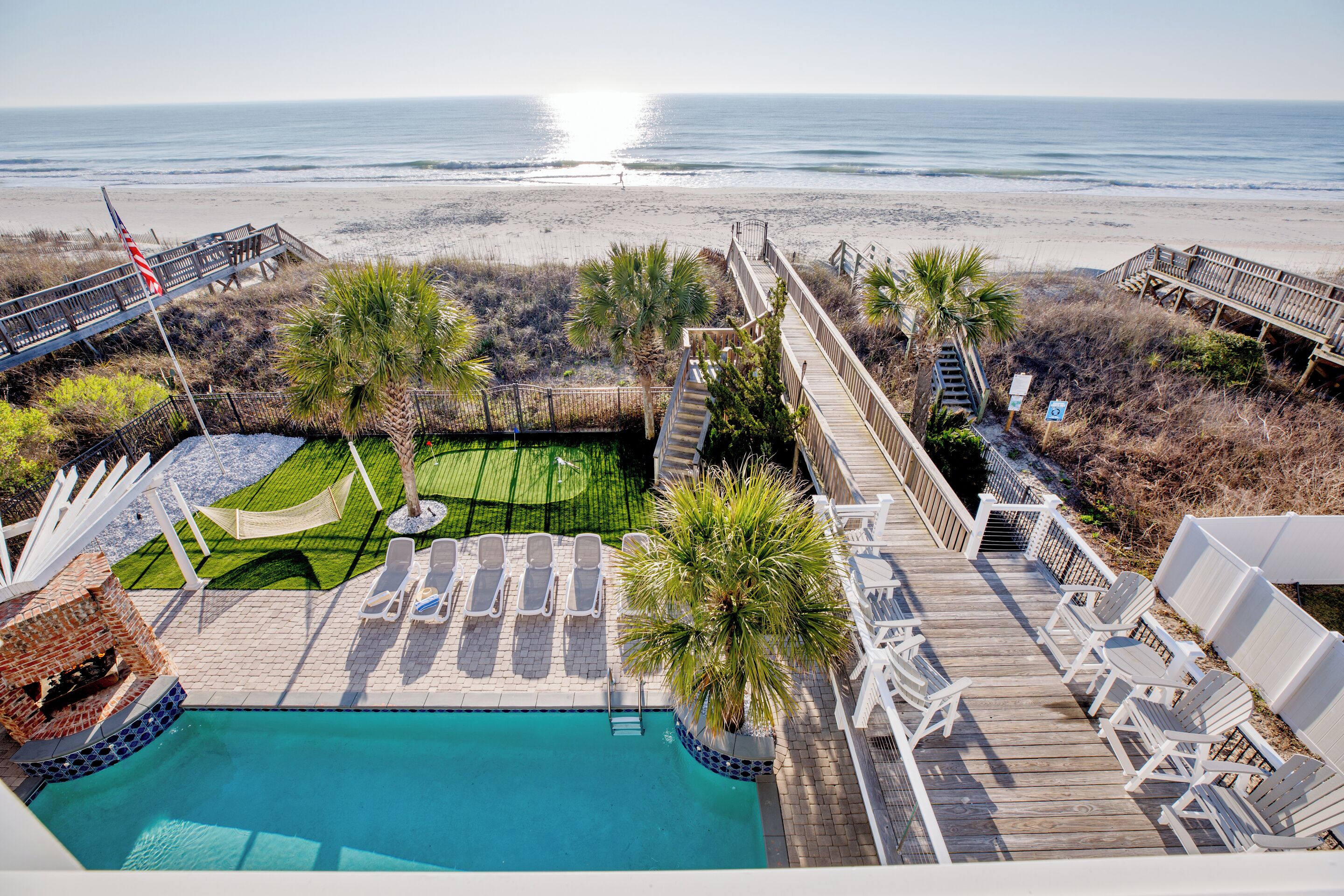Un espace piscine avec vue sur la plage, une terrasse en bois, des chaises longues et un drapeau.