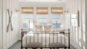 A bedroom with a bed, a window with blinds, a view of the sea, and a wall-mounted lamp. - Grey Goose: Oceanfront Escape, Backyard Oasis + Prime Location (Murrells Inlet)