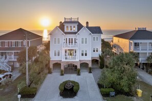 A two-story house with a balcony, a driveway, and a small fountain in the center.