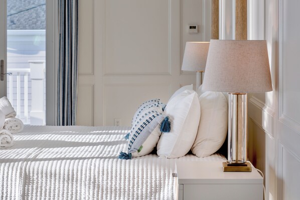 A neatly made bed with rolled towels, a bedside lamp, and a view through a window.
