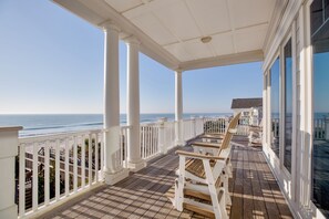 A covered outdoor area with a wooden deck, white railings, and a view of the ocean.