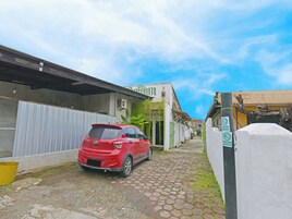 Una estrecha calle adoquinada con un auto rojo estacionado en la acera, un edificio con un letrero que dice 'HOTEL BBL' y un árbol con enredaderas colgantes.