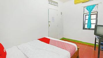 A room with a bed, a television, a door, and a window with curtains.