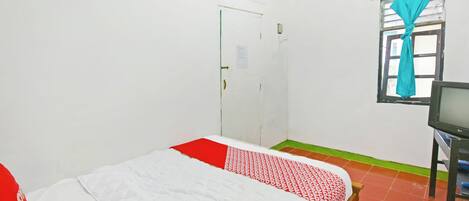 A room with a bed, a television, a door, and a window with curtains.