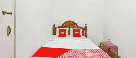 Habitación con una cama individual, cabecera de madera, dos almohadas rojas con la marca 'OYO', edredón blanco acolchado y manta con diseño rojo y blanco.