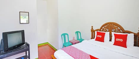 A hotel room with a bed, a television on a stand, a small table with a chair, and a red and white patterned bedspread.