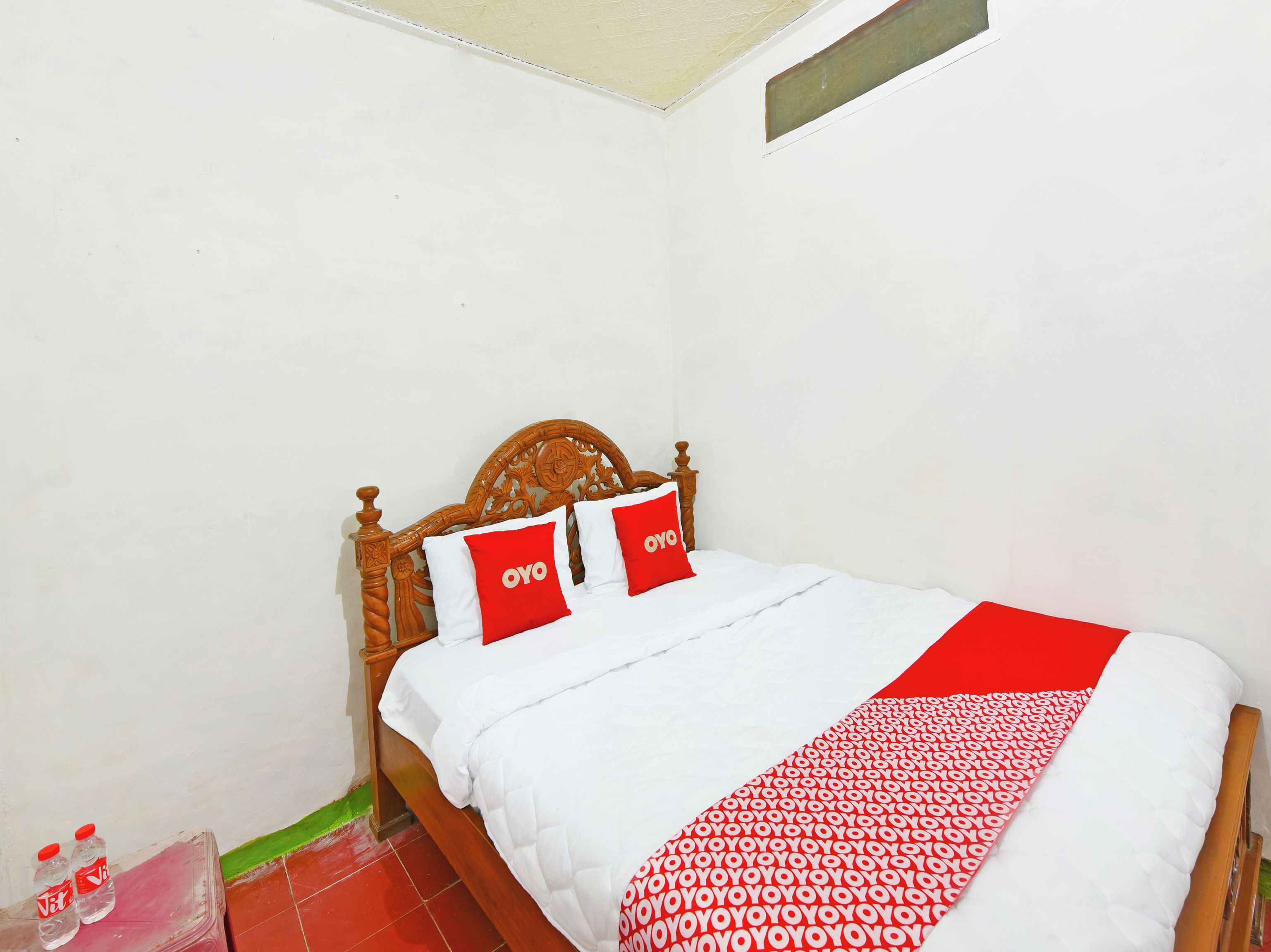 Uma cama com cabeceira de madeira, duas almofadas com a marca 'OYO', um edredom branco e um cobertor vermelho e branco estampado.