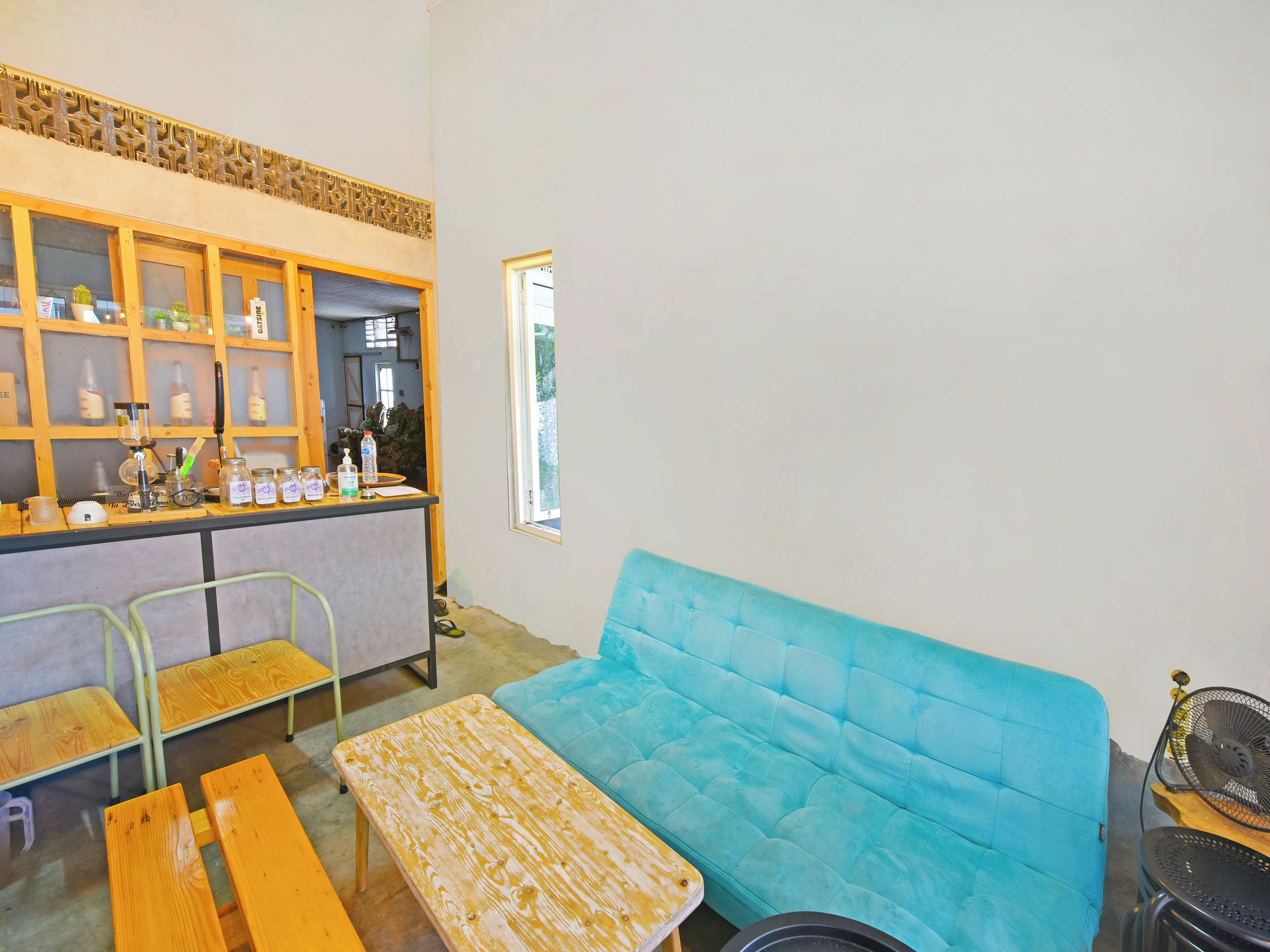 Una habitación con un sofá azul, mesas de madera, una zona de bar con frascos y botellas de vidrio, y una ventana.