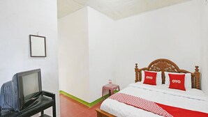 Una habitación de hotel con una cama de madera, un televisor sobre un soporte negro y una mesita con un taburete rosa.
