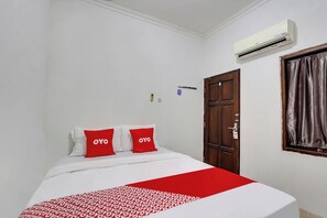Ein Hotelzimmer mit einem Bett, rot-weißer Bettwäsche, einer Klimaanlage, einer Holztür und einem Vorhangfenster.