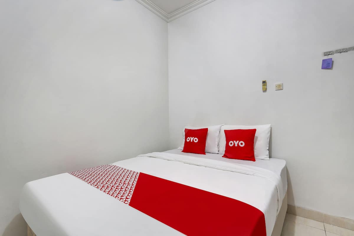 Ein Hotelzimmer mit einem Bett, weißen Wänden und einer rot-weißen Tagesdecke.