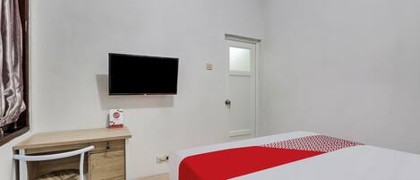 A hotel room with a bed, a desk with a chair, a television mounted on the wall, and a door.
