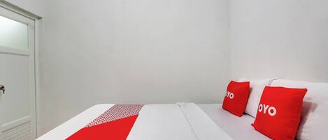 A hotel room with a bed, two red pillows with the word "YOYO" on them, a white and red bedspread, and a white door.