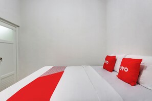 Ein Hotelzimmer mit einem Bett, zwei rote Kissen mit dem Aufdruck 'YOYO' und einer weißen, roten Bettdecke sowie einer weißen Tür.