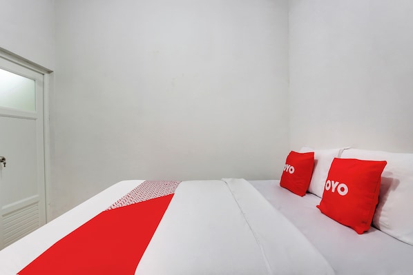 Une chambre d’hôtel avec un lit, deux oreillers rouges, un couvre-lit blanc et une porte blanche.