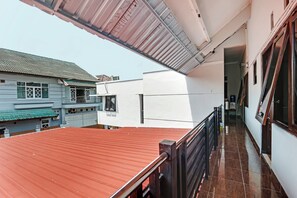 Un edificio residencial con techo rojo, paredes blancas y un balcón con barandilla metálica.