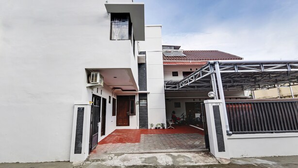 A modern building with a gated entrance, a covered area, and a red-tiled roof visible in the background.