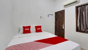 A hotel room with a bed, red and white bedding, an air conditioner, a wooden door, and a window with curtains.